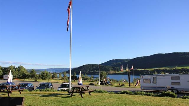Utsikt over en innsjø med fjell i bakgrunnen, flagg og campingvogn i forgrunnen.