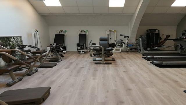Treningsrom med flere treningsapparater, inkludert benkpress, tredemøller og styrketreningsutstyr.