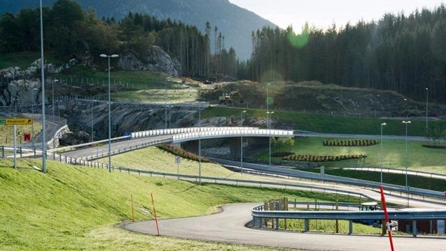 En svingete vei med grønt gress og fjell i bakgrunnen, omgitt av lys og moderne veibelysning.