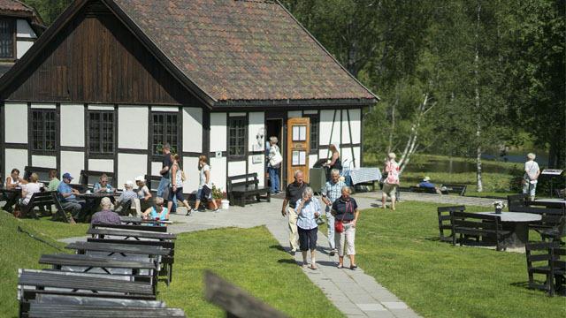 En koselig kafé med folk som sitter ute, og besøkende som går mot inngangen i et naturskjønt område.