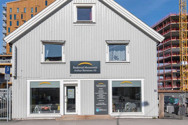En grå bygning med butikkvinduer og skilt for "Balansed Merker" i en bygate. Bygningen har to etasjer.