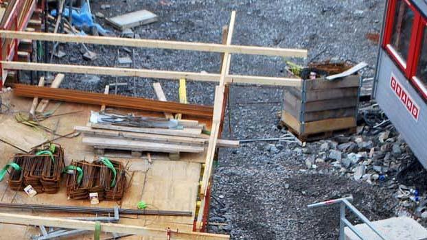 Byggeplass med treplanker, stålstenger og en kasse på bakken. Uferdig konstruksjon med byggeutstyr.