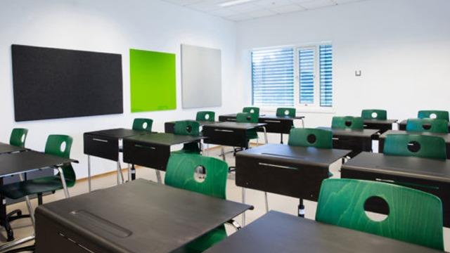 Moderne klasserom med svarte og grønne tavler, grønne stoler og svarte pulter i et lyst rom.