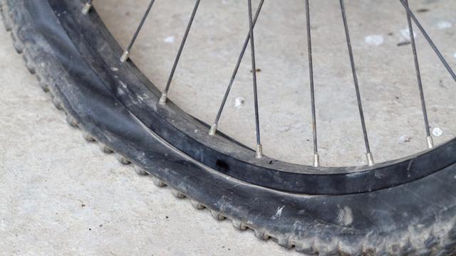 En punktert sykkelhjul med synlig dekk og eiker på en betongoverflate.
