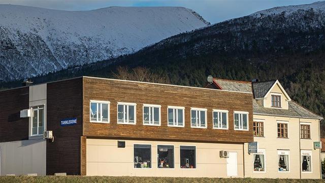 Moderne bygning med store vinduer og en tradisjonell bygning ved foten av snødekte fjell.