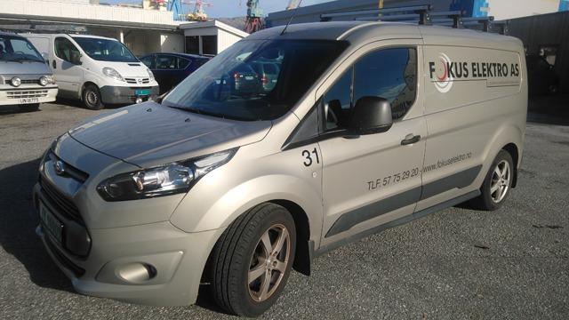 En grå varebil med påskrift "Fokus Elektrisk" parkert på en gårdsplass.