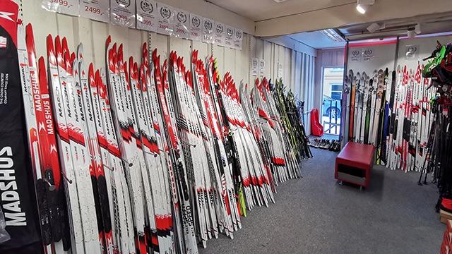 En butikk med mange langrennsski på rekke, med røde og hvite detaljer, og en rød benk i midten.