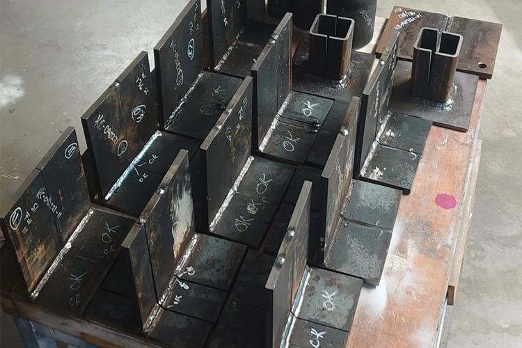 Sveisede metallplater og profiler stablet på en arbeidsbenk i et verksted.