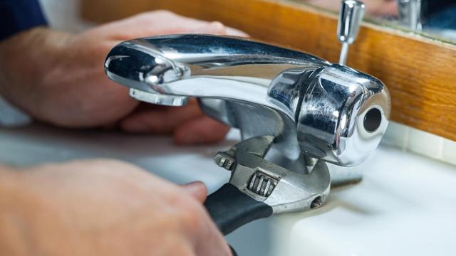 En person bruker en skiftenøkkel for å fikse en kran på et vaskeservant.