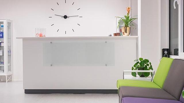 Moderne resepsjon med klokke, planter og en fargerik sofa i et lyst rom.