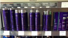 Hyller med Redken hårprodukter i lilla flasker, inkludert sjampo og balsam, på en salong.