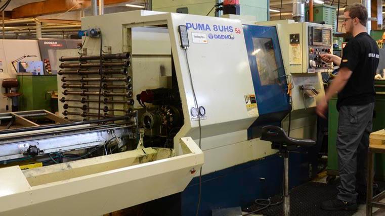 En operatør jobber ved en moderne CNC-maskin i en fabrikk, med fokus på presisjonsproduksjon.