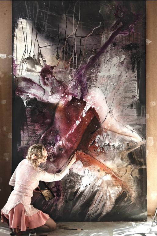 Kvinne i rosa kjole maler et stort abstrakt kunstverk med røde og lilla farger.