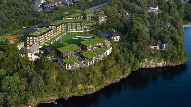 Moderne hotellkompleks med grønt tak, beliggende ved vannkanten og omkranset av frodig natur.