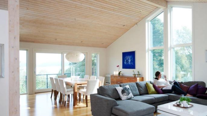 Moderne stue med høyt tak, store vinduer, en sofa, et spisebord og en person som sitter og leser.