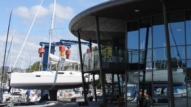 Moderne marina med en seilbåt hevet av kraner og en glassbygning i forgrunnen.