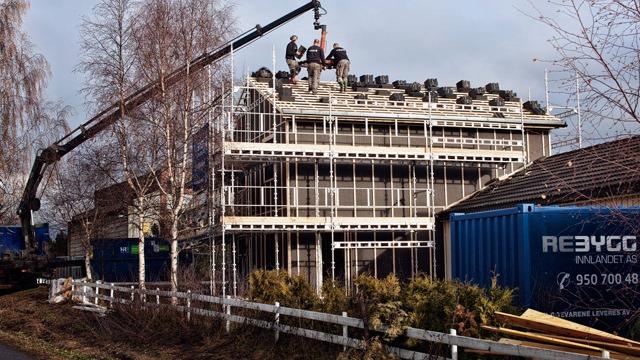 Bygning under rehabilitering med arbeidere på taket, heisekran og stillas rundt.