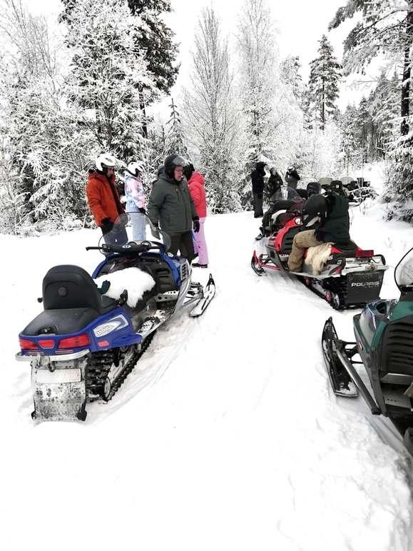 Grupp mennesker står ved snøscootere i snødekt skog, klare for en vinterutflukt.