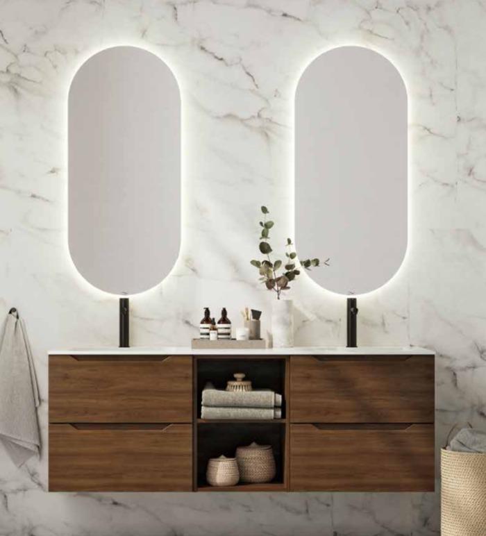 Moderne bad med to speil med lys, en trekommode og dekorative planter på benken.