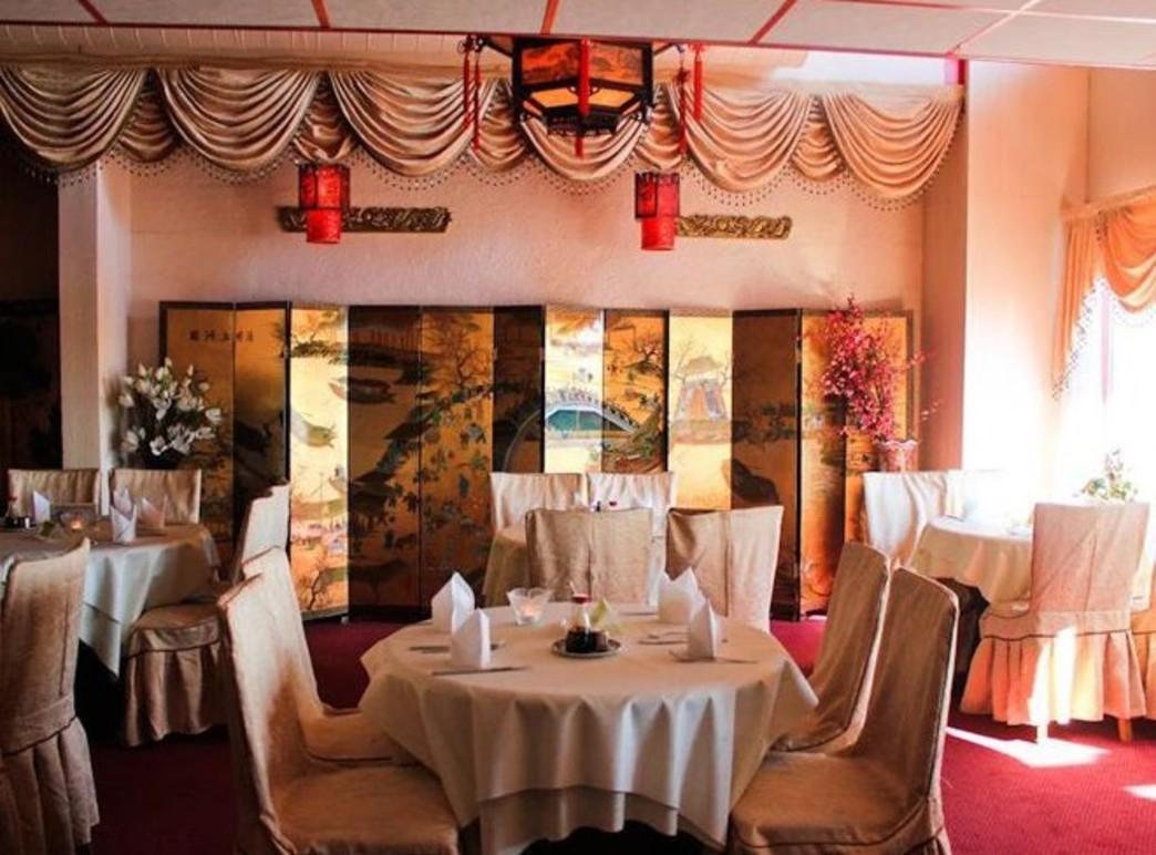 Elegant restaurantinteriør med runde bord, hvite duker og dekorative veggpaneler. Røde lanterner henger fra taket.