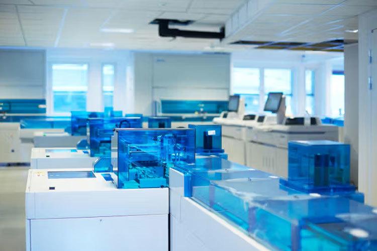 Moderne laboratorieutstyr med blå plastbeholdere i et lyst rom med vinduer og datamaskiner.