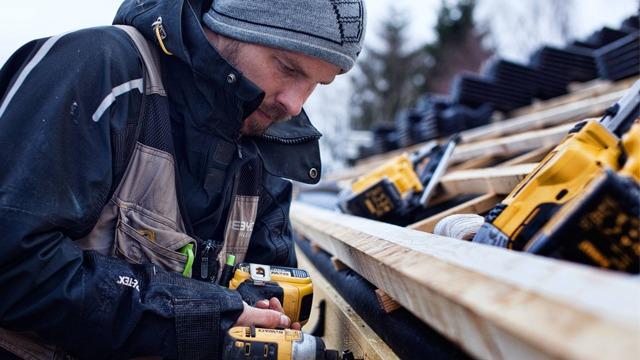 En håndverker som bruker en drill på et tak med verktøy og materialer i bakgrunnen.