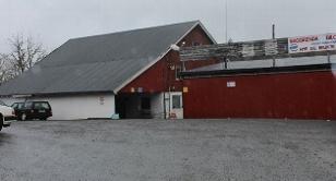 Rødt lagerbygg med grått tak og parkerte biler på en grå dag.
