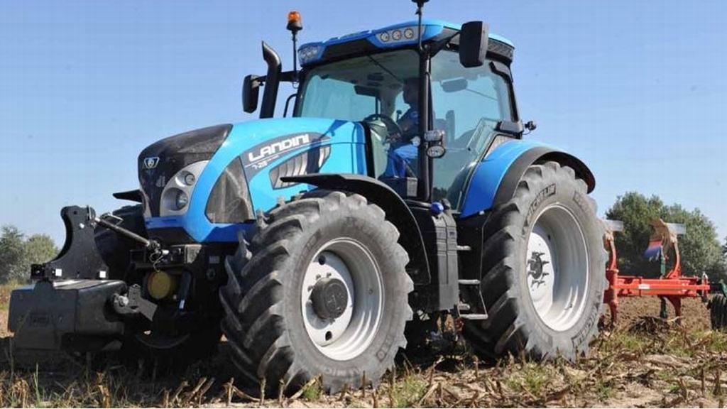 Blå traktor med store dekk står på en åker, klar til å pløye jorden.