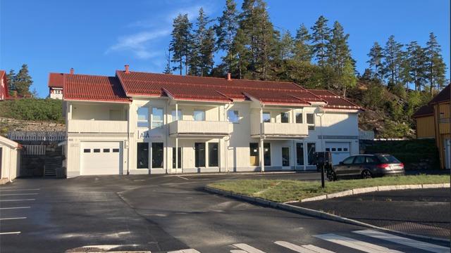 Moderne tomannsbolig med rød takstein, garasje og grønt område i bakgrunnen. Solfylt dag med blå himmel.