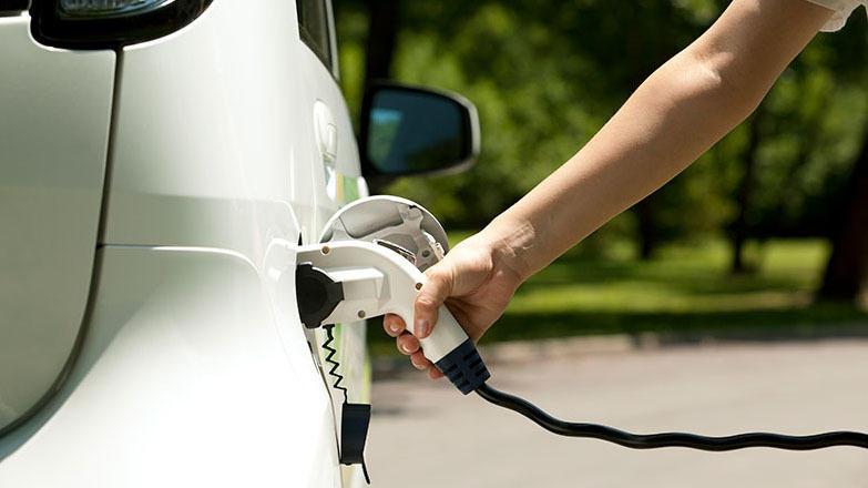 En person lader en elektrisk bil med en ladekabel i en park.