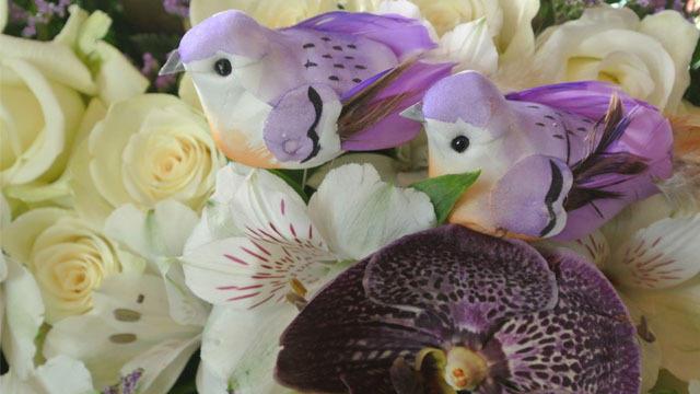 Fargerike fugler i en blomsterbukett med hvite roser og liljer.