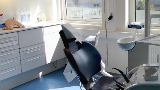 Tannlegekontor med en tannlegestol, vask og medisinske verktøy i et lyst rom.