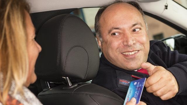 En smilende mann gir et kredittkort til en kvinne i bilen. De ser ut til å ha en vennlig samtale.