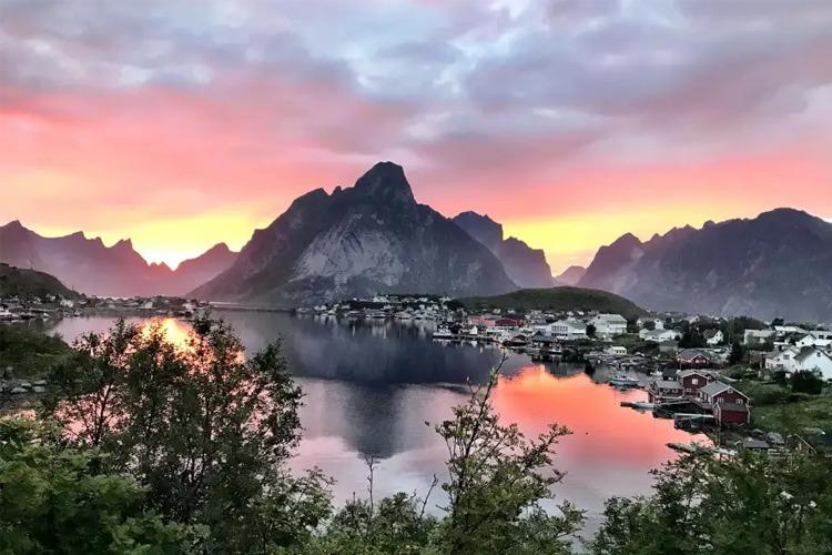 En vakker solnedgang over fjellene og en liten by ved vannet i Norge. Fargene reflekteres i vannet.