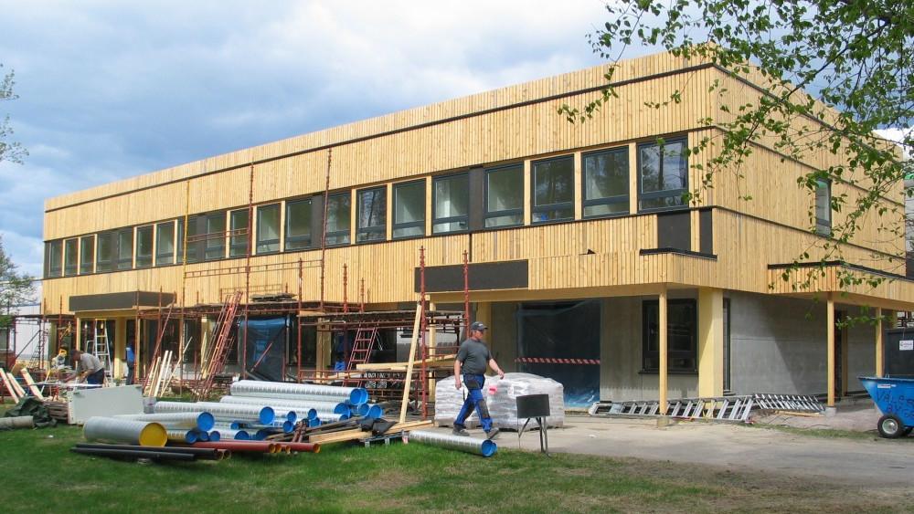 Moderne bygning under konstruksjon med trepanel, stillas og byggeutstyr på en grønn plen.