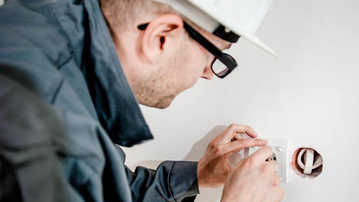 En elektriker installerer en stikkontakt på en hvit vegg.