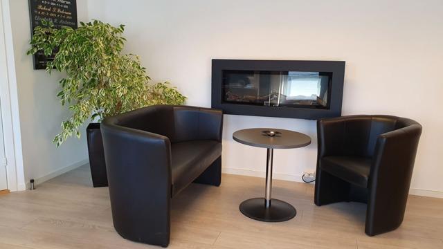 To sittegrupper med svarte stoler og et rundt bord foran en moderne peis i et lyst rom.