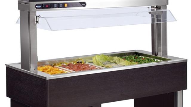 En moderne buffé med glasslokk og flere grønnsaks- og salatretter i ulike farger.