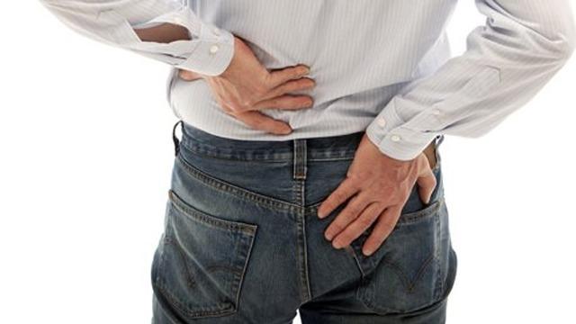 Mann som holder seg på ryggen, viser tegn på ryggsmerter, iført skjorte og jeans.