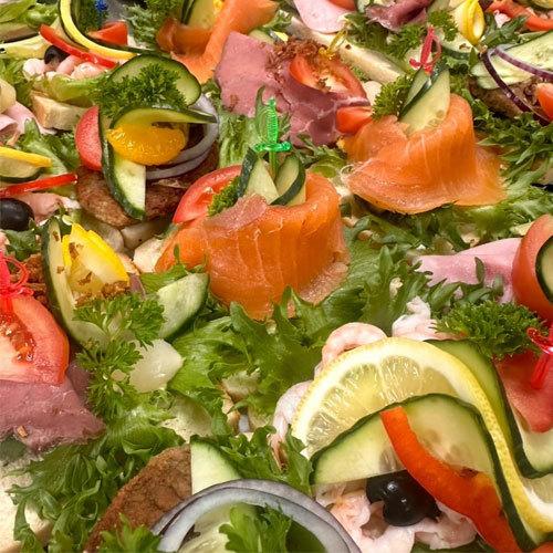 Fargerik koldtbord med røkt laks, skinke, reker, grønnsaker og friske urter på en seng av salat.
