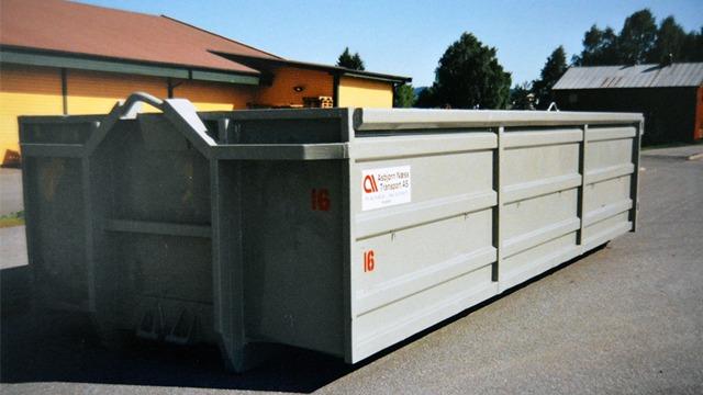 En stor grå container plassert på en asfaltvei, med bygninger i bakgrunnen.