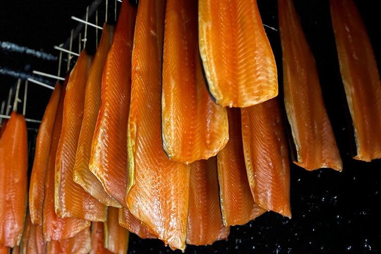 Røkt laks henger til tørk i et mørkt rom, med glinsende oransje fileter på trestenger.