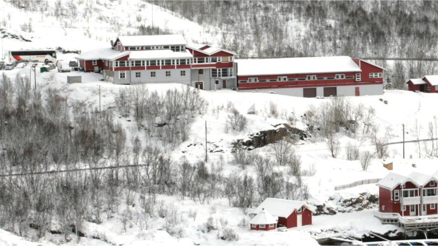 Rødt hotell med snødekte tak og trær i vinterlandskapet, omgitt av fjell og skog.