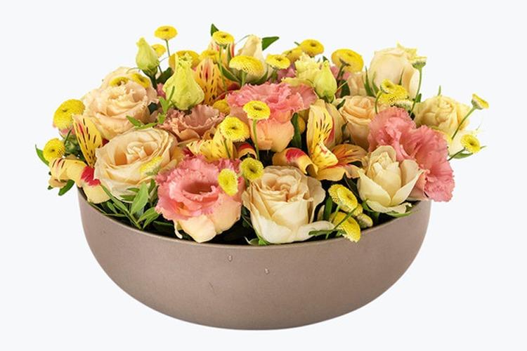 En vakker blomsteroppsats med roser, alstromeria og nelliker i en rund vase.