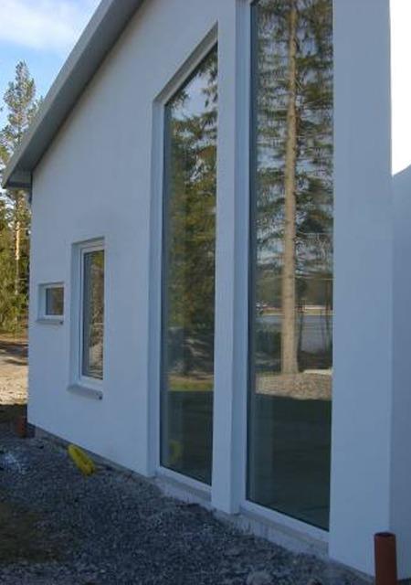 Moderne husvegg med store vinduer og trær i bakgrunnen, beliggende i et naturskjønt område.