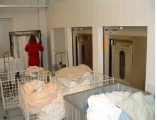 En person i rød uniform som jobber med klesvask i et vaskerom med flere vaskemaskiner og kleskurver.