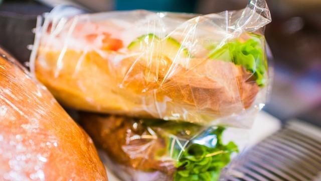 En innpakket sandwich med salat og tomat, plassert på en arbeidsbenk med brød i bakgrunnen.