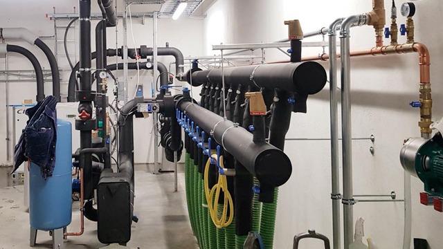 Rørleggerarbeid med svarte rør, vannpumper og tilkoblinger i et industrielt rom.