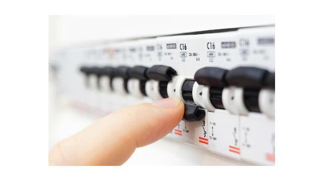 En hånd som justerer en bryter på et elektrisk sikringsskap med flere kontroller.