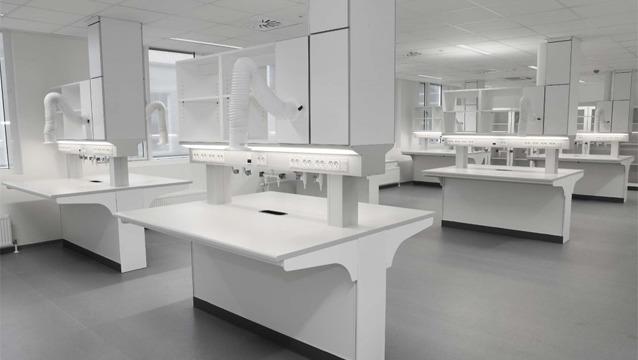 Moderne laboratoriemiljø med hvite arbeidsbenker og ventilasjonskapper i et lyst rom.